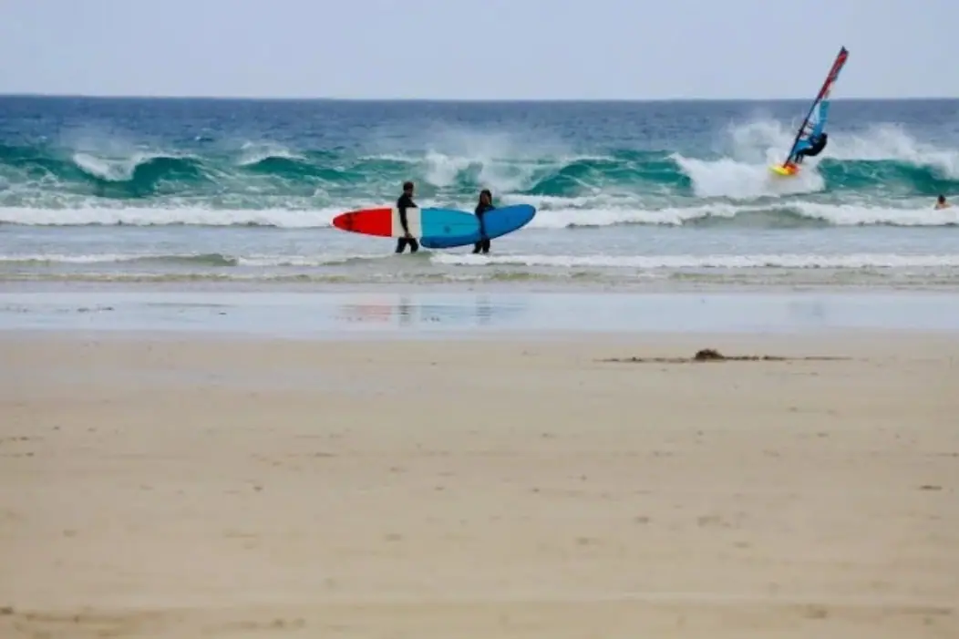 Surfers and a kitesurfer on the beach at Sandy Point
